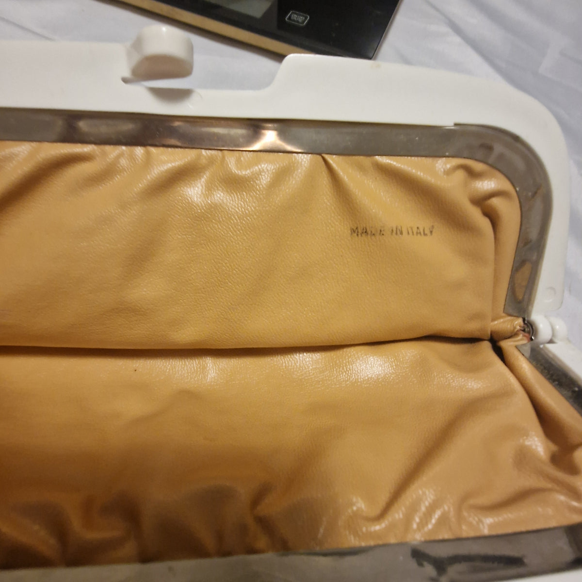 Open clutch showing tan lining stamped Made in Italy and the cream frame clasp