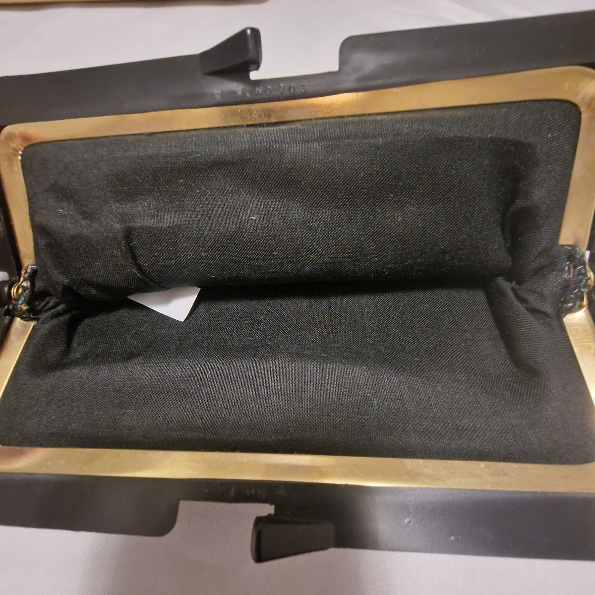 Open black frame bag showing black fabric lining and gold-tone frame, with No. 703 embossed on the shell