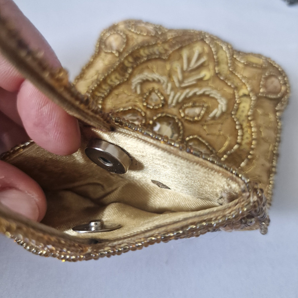 Interior of gold beaded wristlet showing magnetic snap closure and small mark on lining