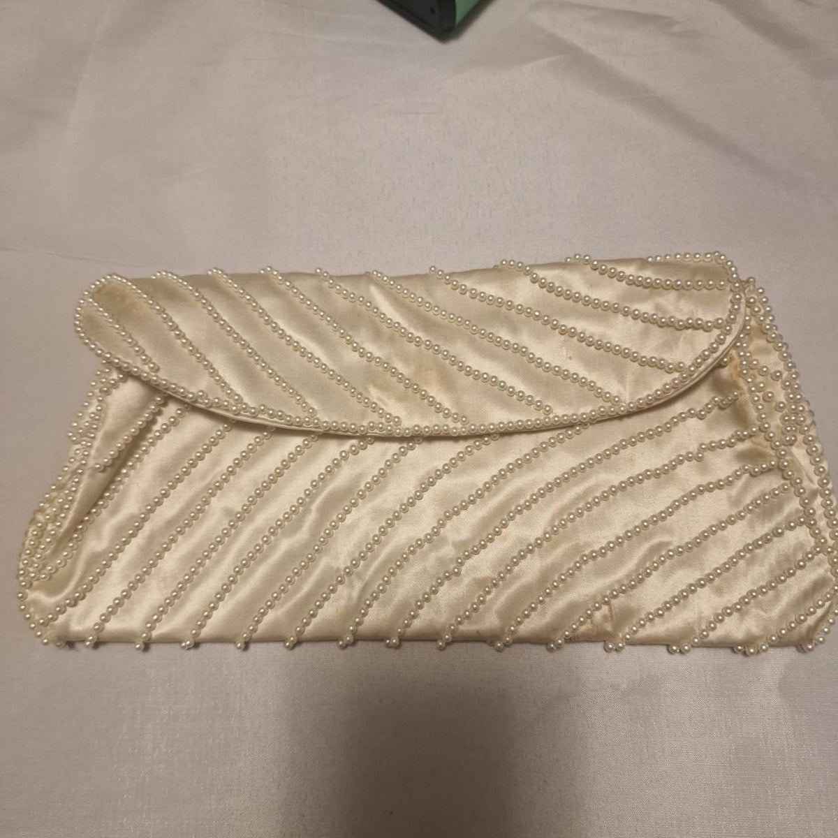 Front of a cream envelope clutch decorated with diagonal rows of faux pearls