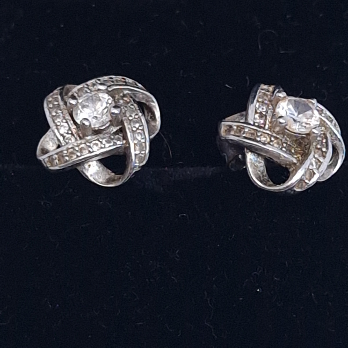Pair of silver-tone love-knot earrings with pave clear stones and a claw-set centre stone on black velvet