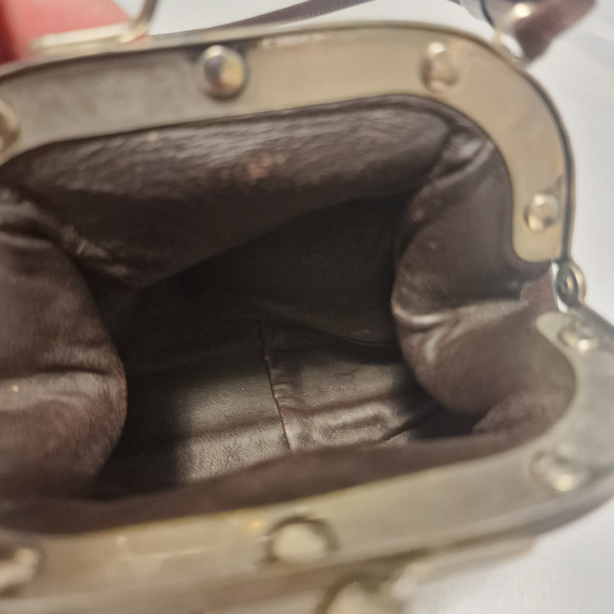 Blurred view inside a brown leather kiss-lock bag showing dark brown lining and riveted silver-tone frame