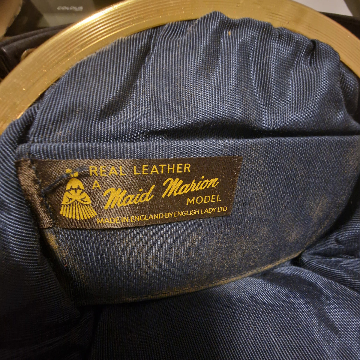 Close-up of the woven Maid Marion Model label inside a navy bag, stating Real Leather and Made in England by English Lady Ltd, on blue ribbed lining