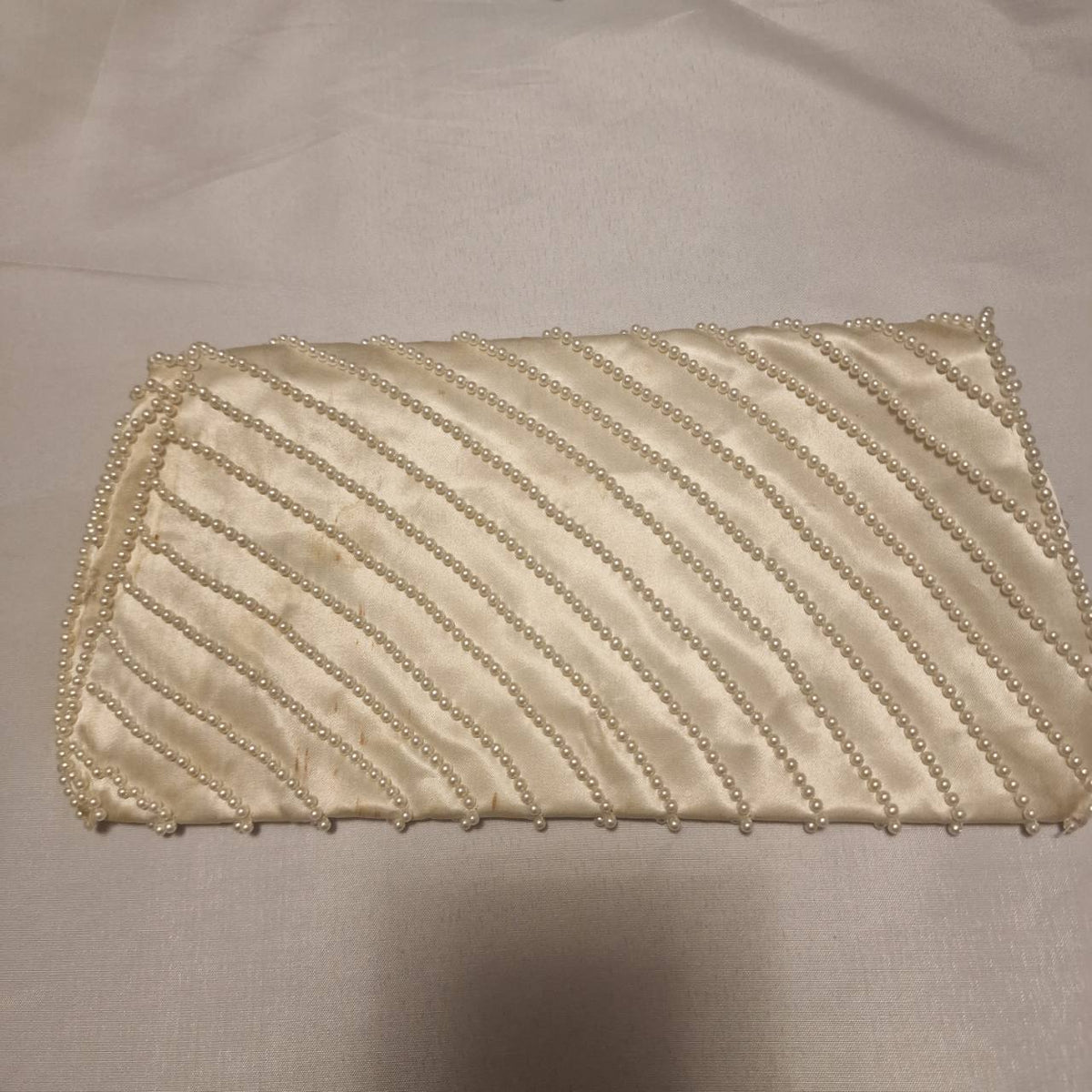 Reverse of the cream faux-pearl clutch showing the pearl-trimmed satin fabric