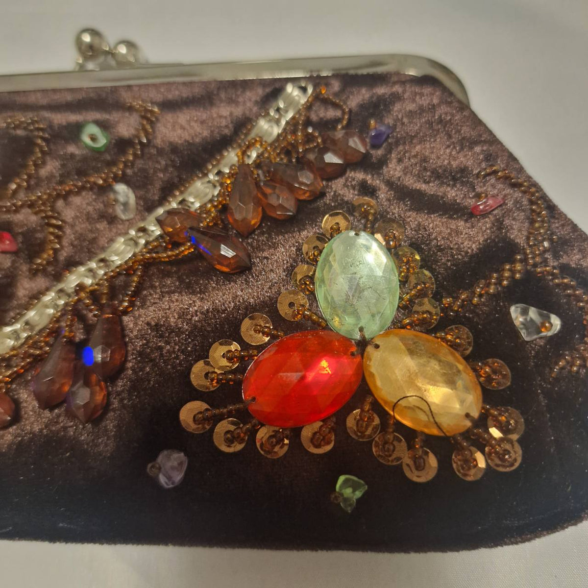 Close-up of green, red and amber faceted stones surrounded by bronze beads on the brown velvet bag
