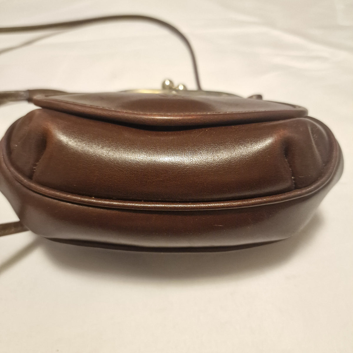 Side view of a brown leather frame bag showing the rounded gusset and piped edge