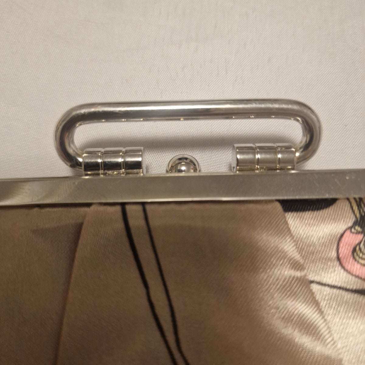 Close-up of the clutch purse's metal handle and its attachment points on the frame.