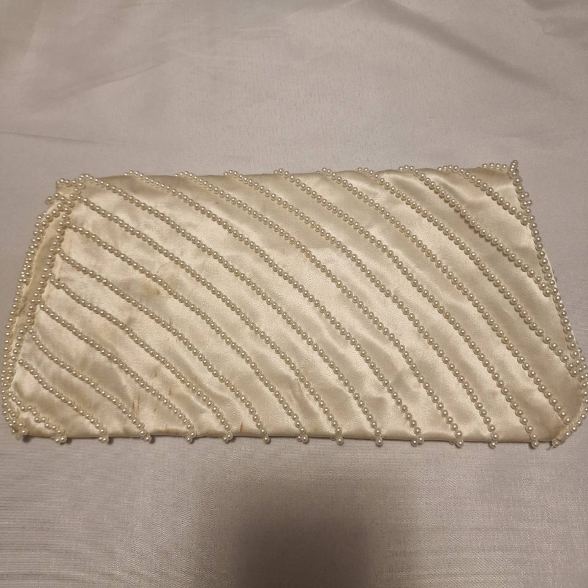 Cream pearl-embellished clutch shown flat to display the full diagonal bead pattern