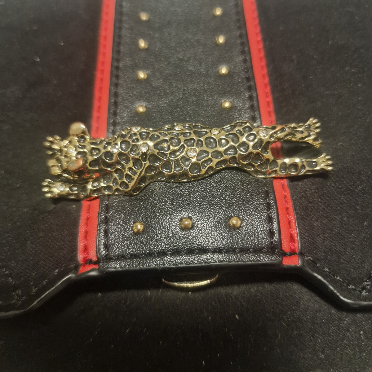 Close view of the leopard-shaped metal-tone ornament across the bag's red-edged black front panel.