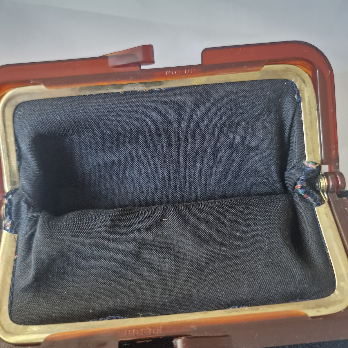 Open frame purse viewed from above, showing black lining, gold-coloured inner frame channels and moulded lettering.