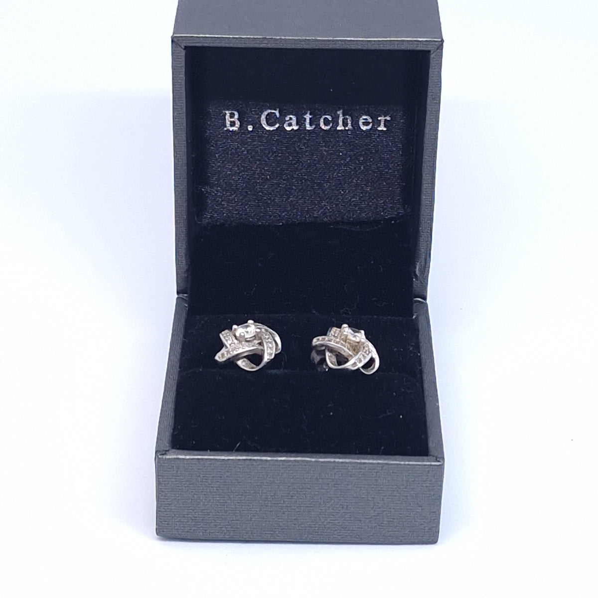 Open presentation box with a pair of silver-tone knot earrings and a printed B.Catcher pillow