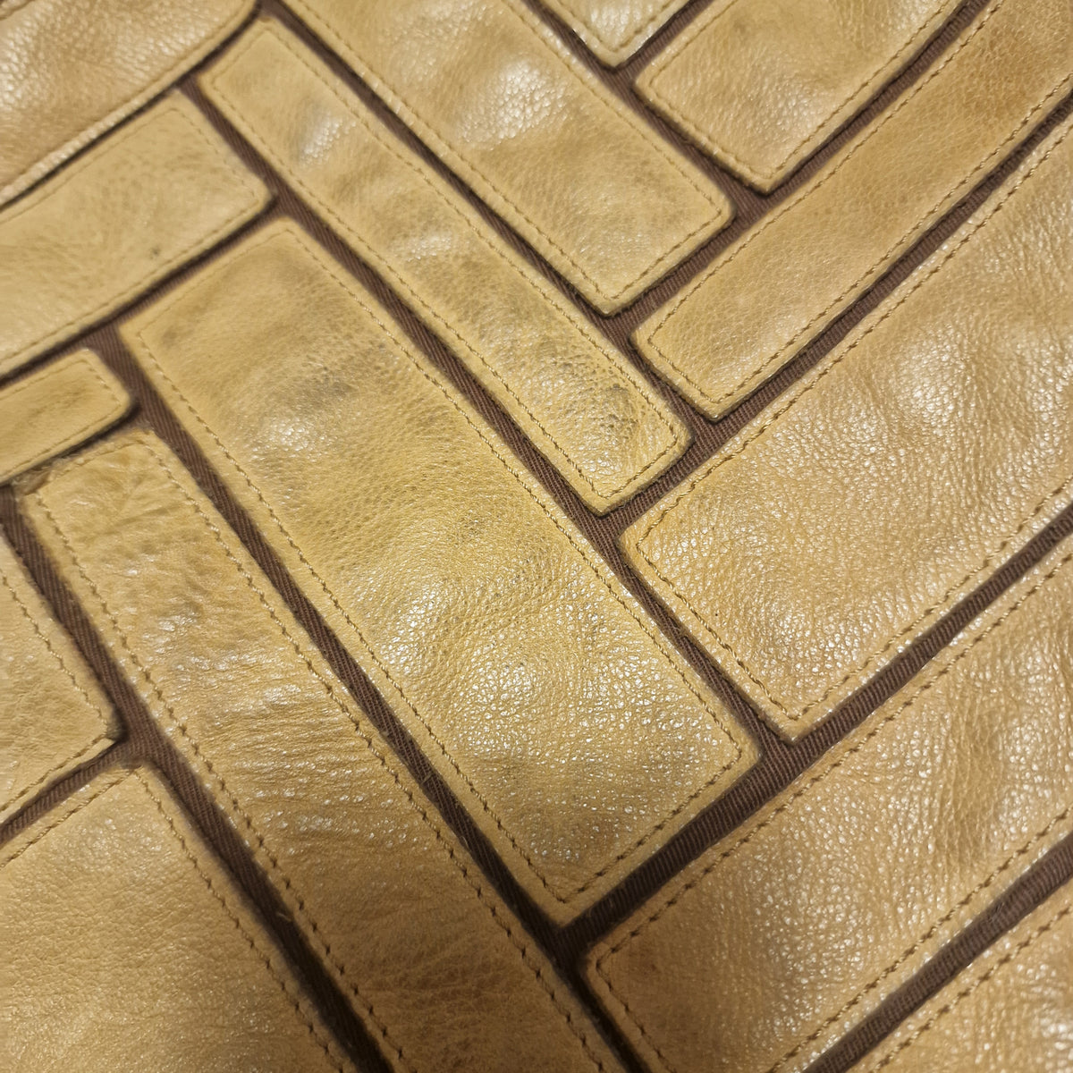 Close-up of tan grained leather rectangles stitched in a herringbone pattern over brown twill