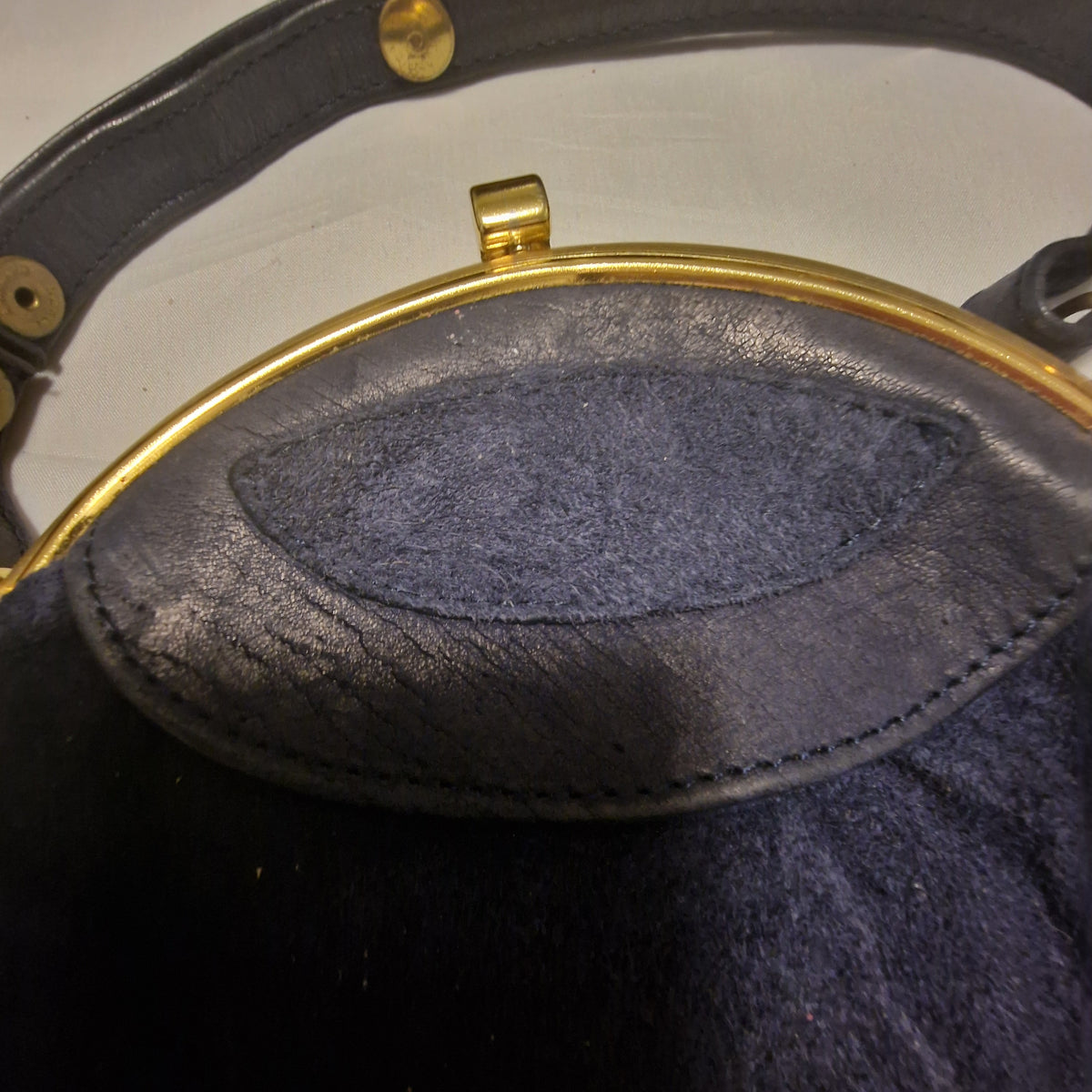 Close-up of the navy leather frame-end panel, gold clasp and snap studs on the handle
