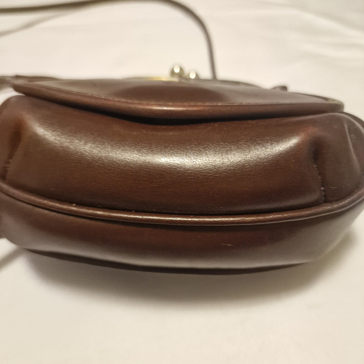 Second side view of the brown leather bag showing the gusset and clasp knobs