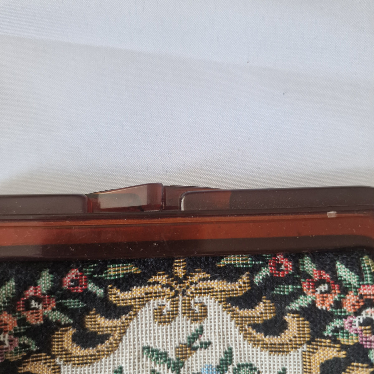 Close-up of the purse's overlapping clasp tabs and translucent reddish-brown upper frame above floral decoration.