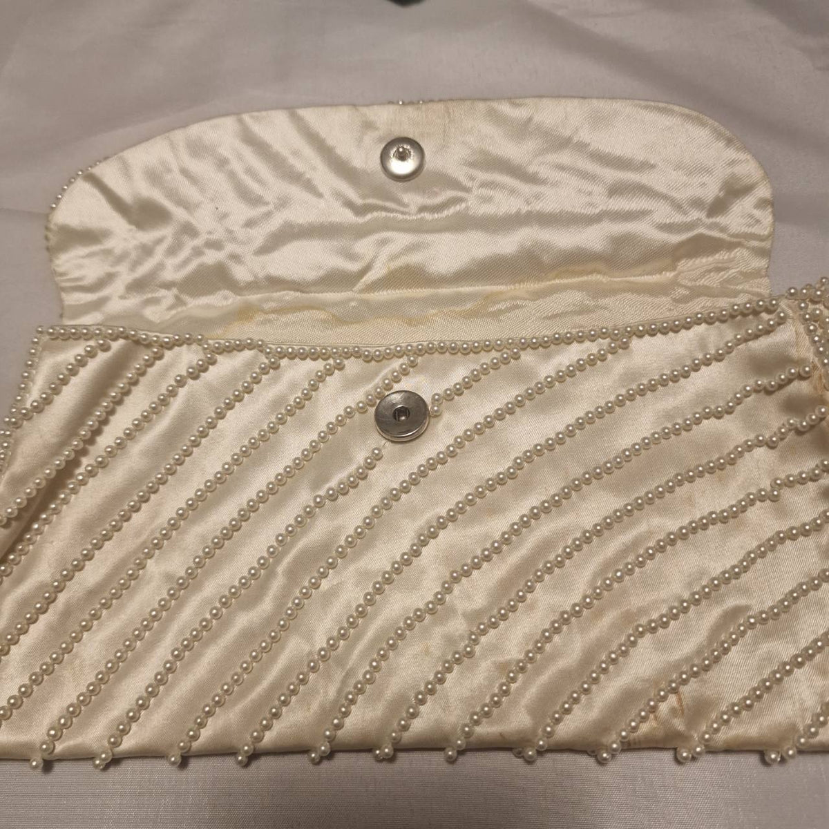 Open cream clutch showing the snap fastening, satin lining and internal slip pocket