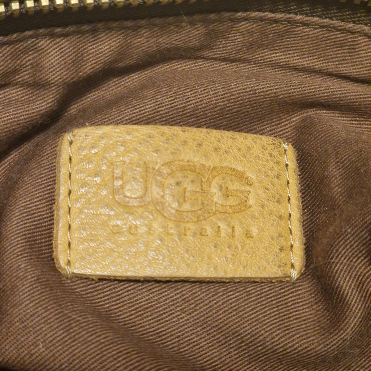 Embossed leather logo tag stitched onto the brown twill lining inside the bag, brass zip teeth at left