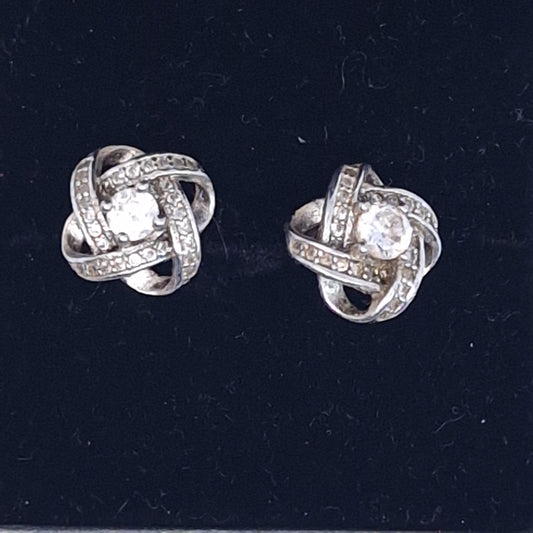 Straight view of two silver-tone interlaced knot earrings with pave bands and a clear centre stone