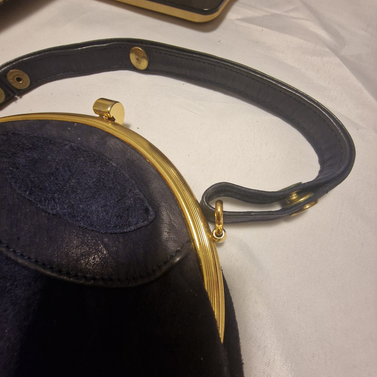 Navy leather handle attached by a gold swivel ring to the ribbed gold-tone frame of a suede bag