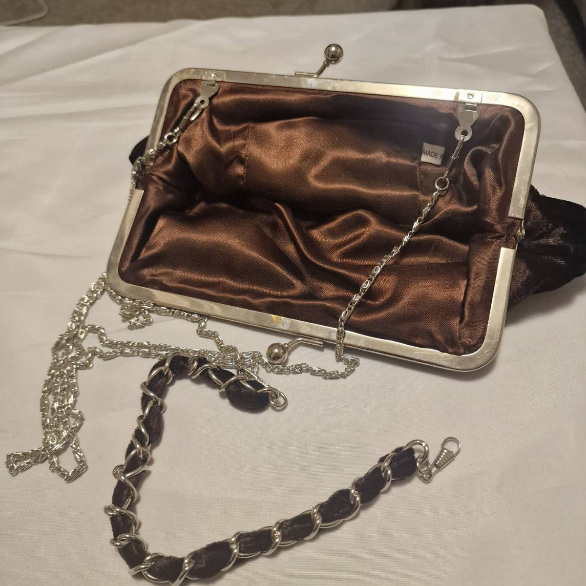 Interior and frame of the brown velvet clutch, showing satin lining and attached chain strap