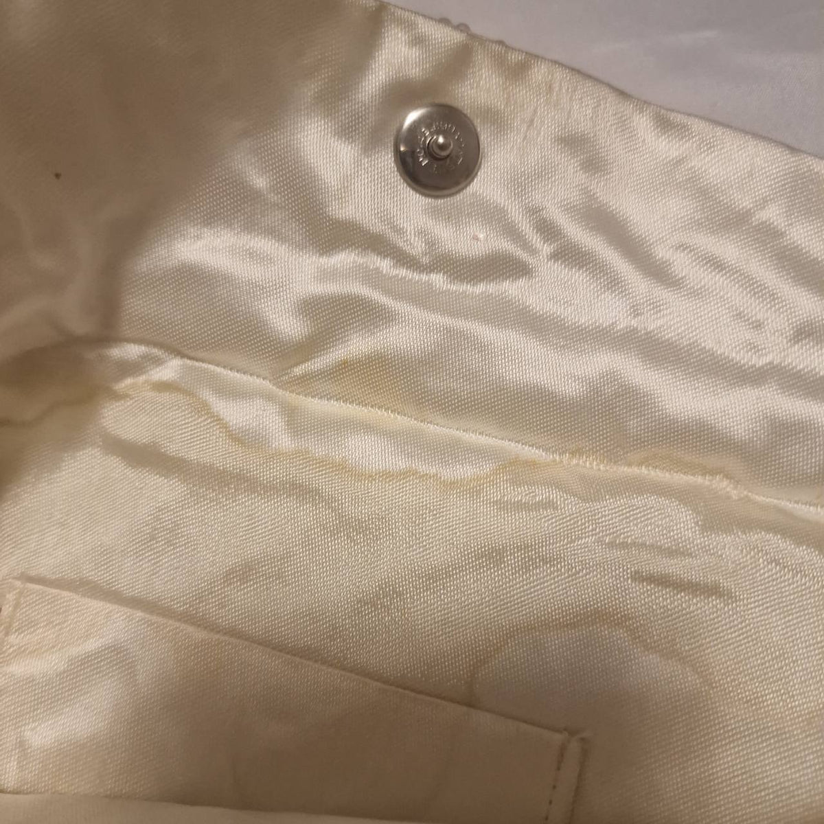 Close view inside the cream clutch showing the lining and yellowish mark