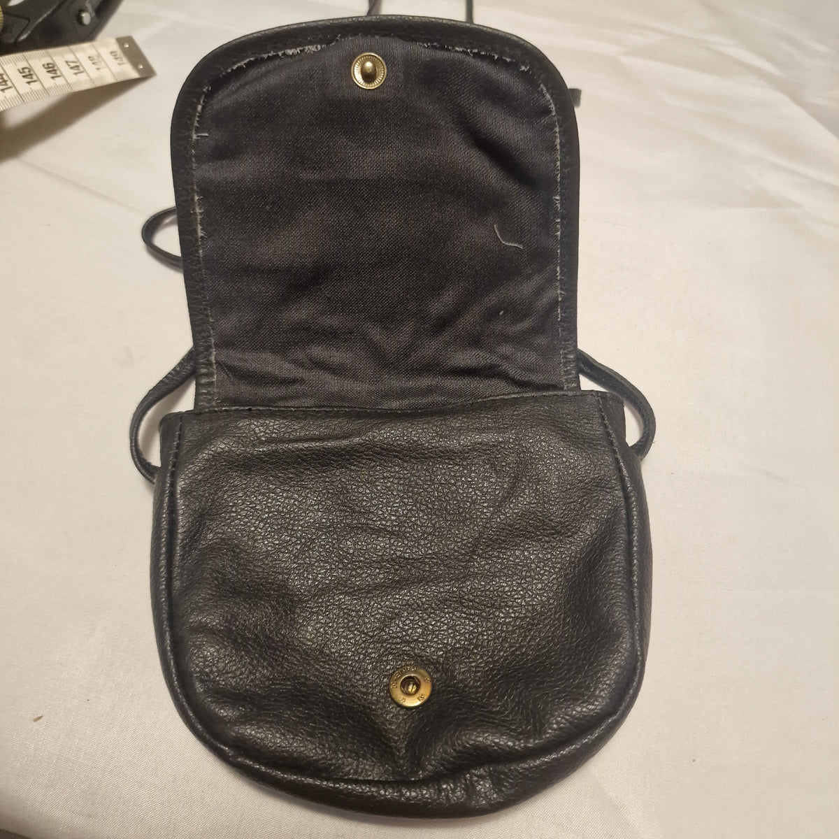 Open black leather bag showing dark fabric lining and a brass-tone snap fastening