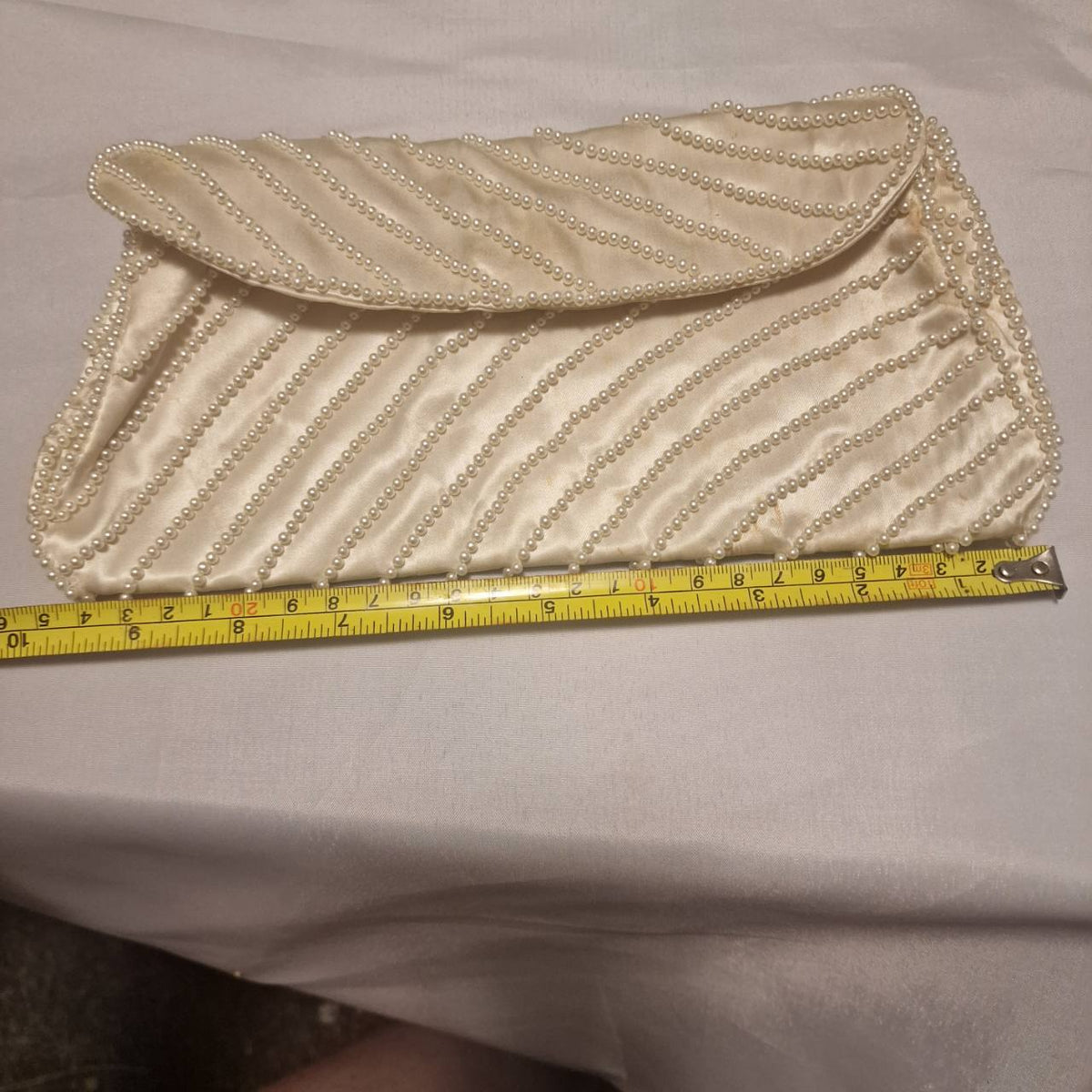 Cream faux-pearl clutch beside a measuring tape showing its approximate width