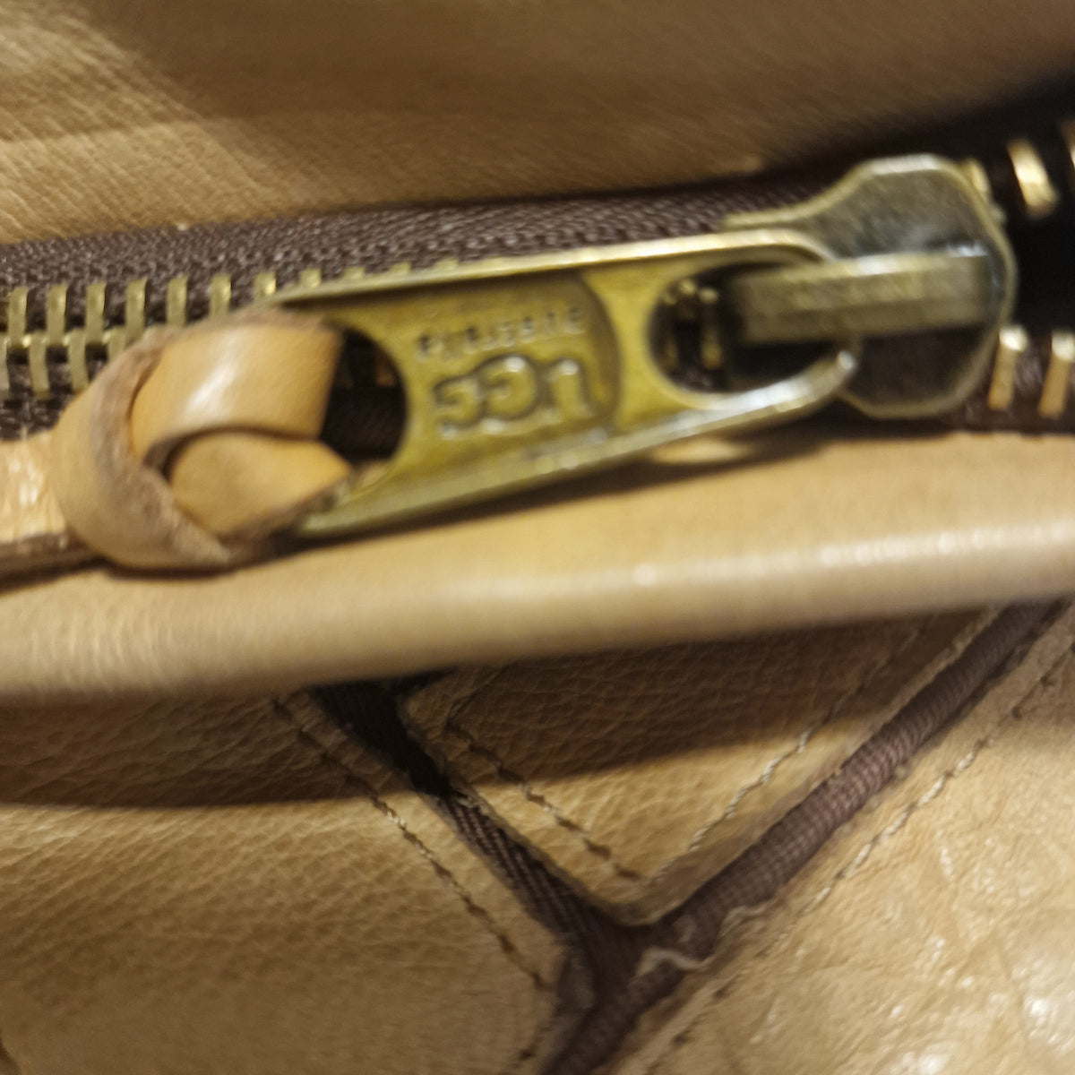 Close-up of the brass-tone UGG-embossed zip pull with a knotted leather tab on a tan leather bag