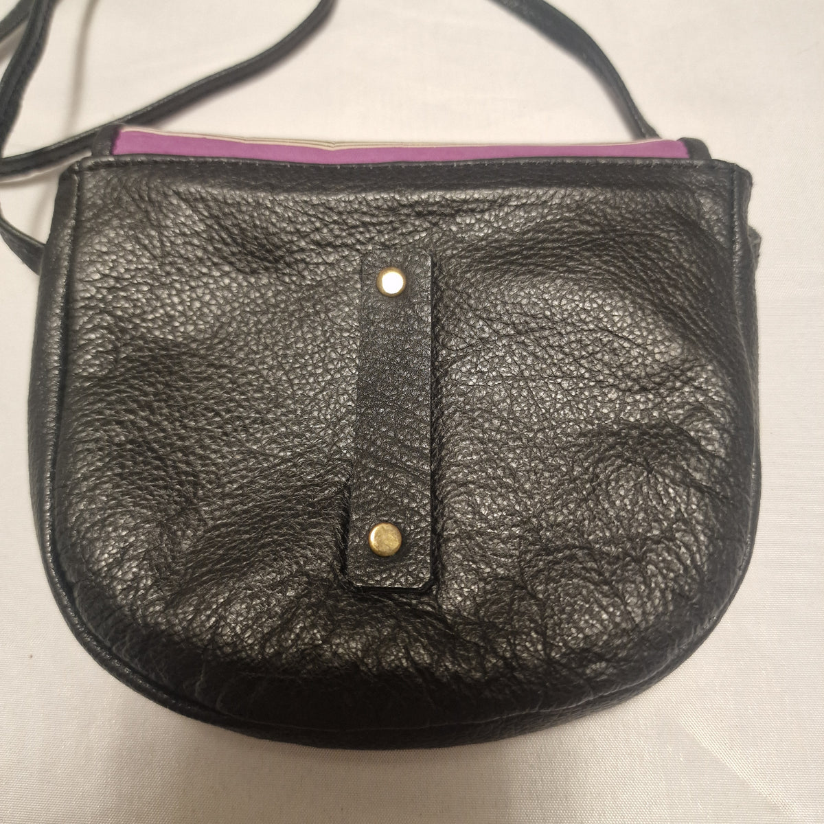 Back of the black pebbled leather bag with a riveted leather tab and thin strap