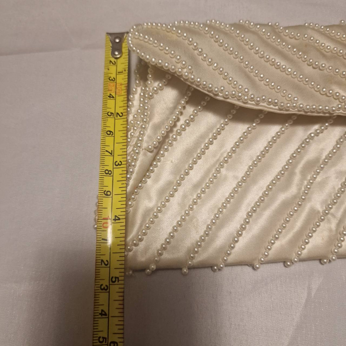 Cream satin clutch beside a measuring tape showing its approximate height