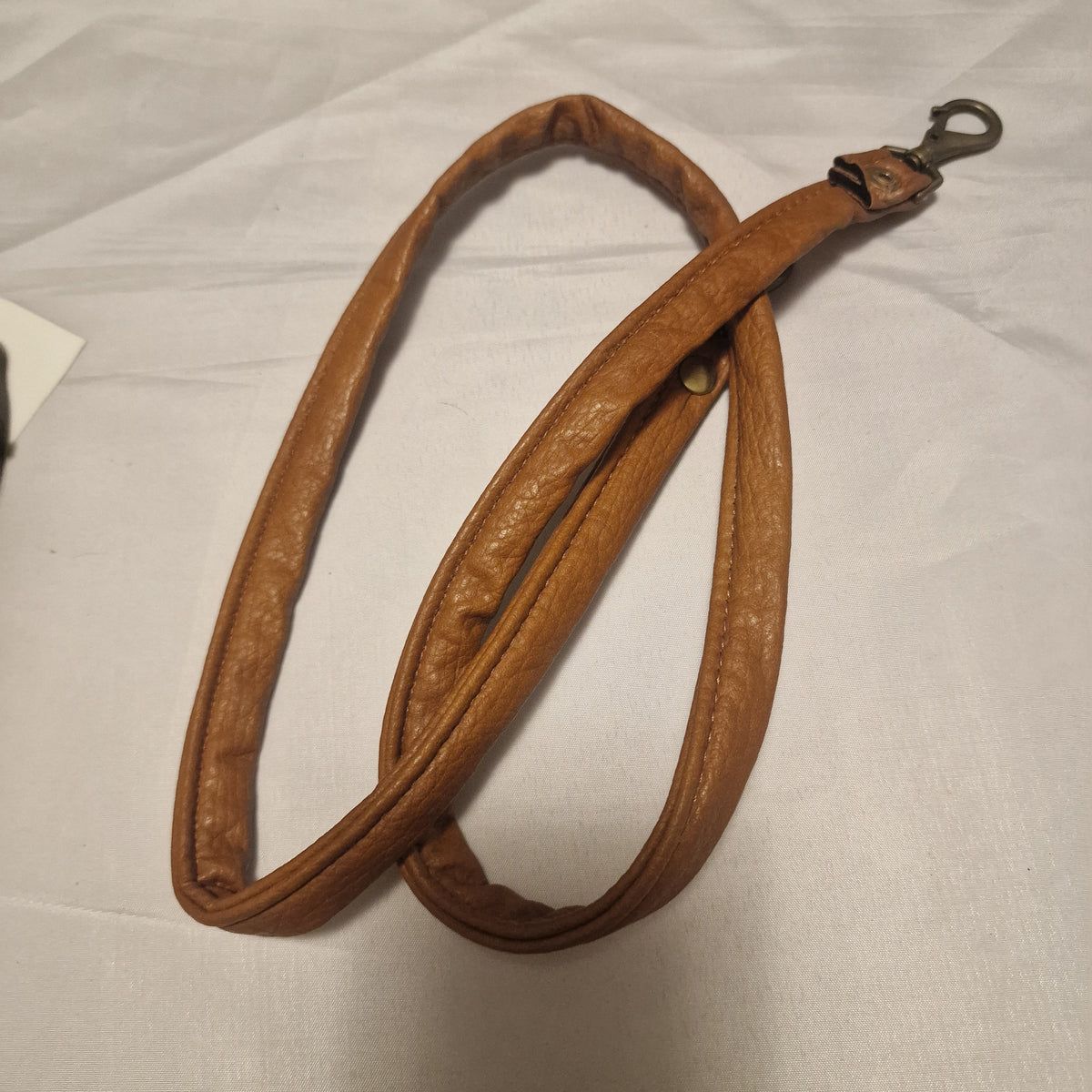 Tan detachable strap with brass-tone swivel clasp and snap, coiled on a white sheet