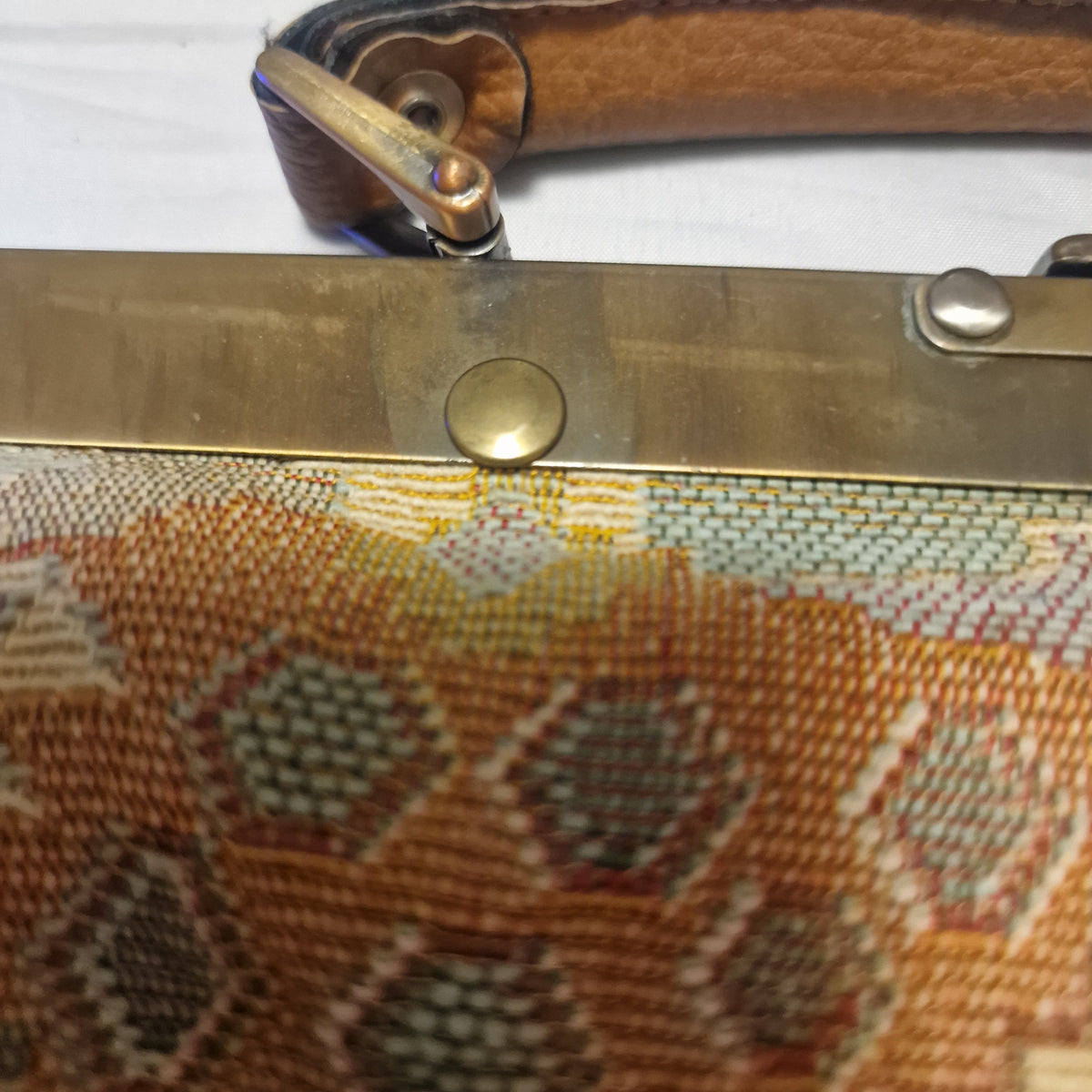 Close view of brass-tone frame, rivet and swivel clip joining the tan handle to the bag