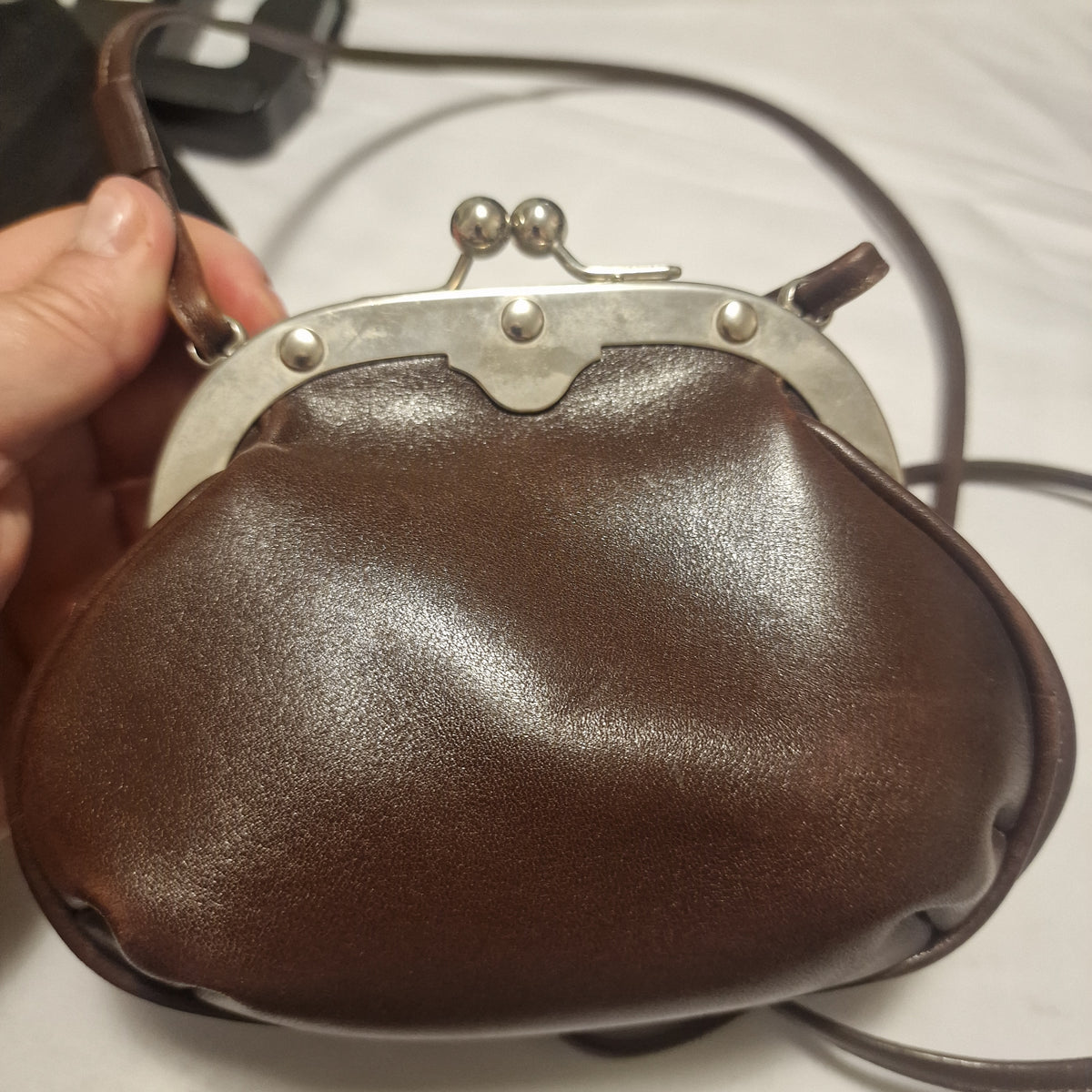 Front of a brown leather kiss-lock bag with silver-tone frame, three rivets and ball clasps