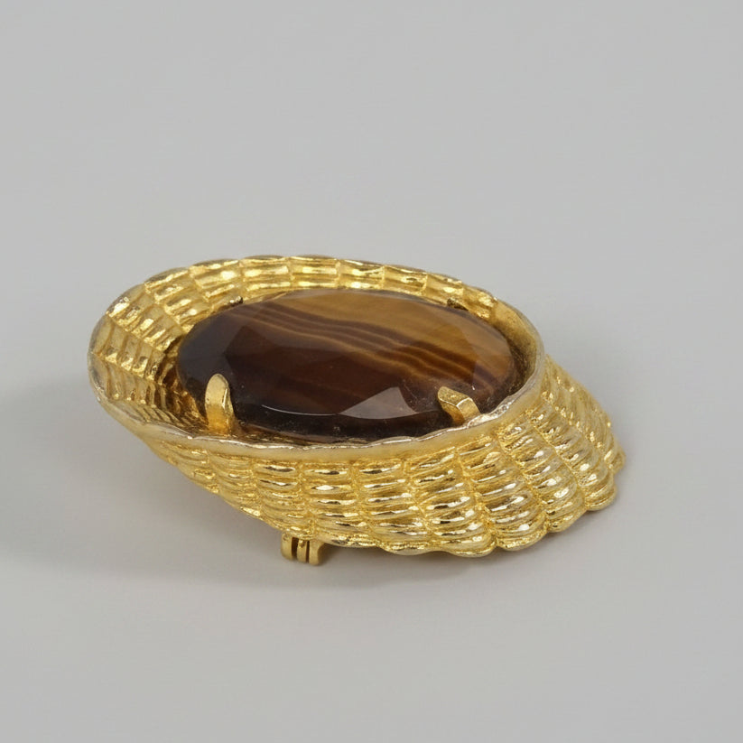 Gold brooch with a dark stone on a marble surface