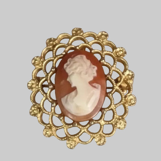 Gold cameo brooch with a red and white stone on a gray background