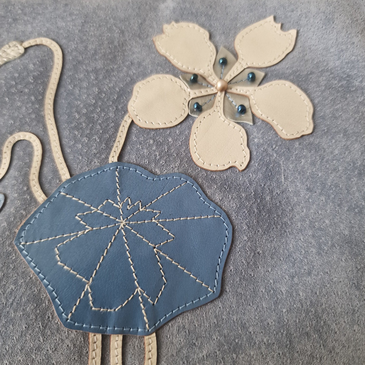 Close-up of stitched cream and blue leather floral appliqué on Barbara Maertens suede clutch