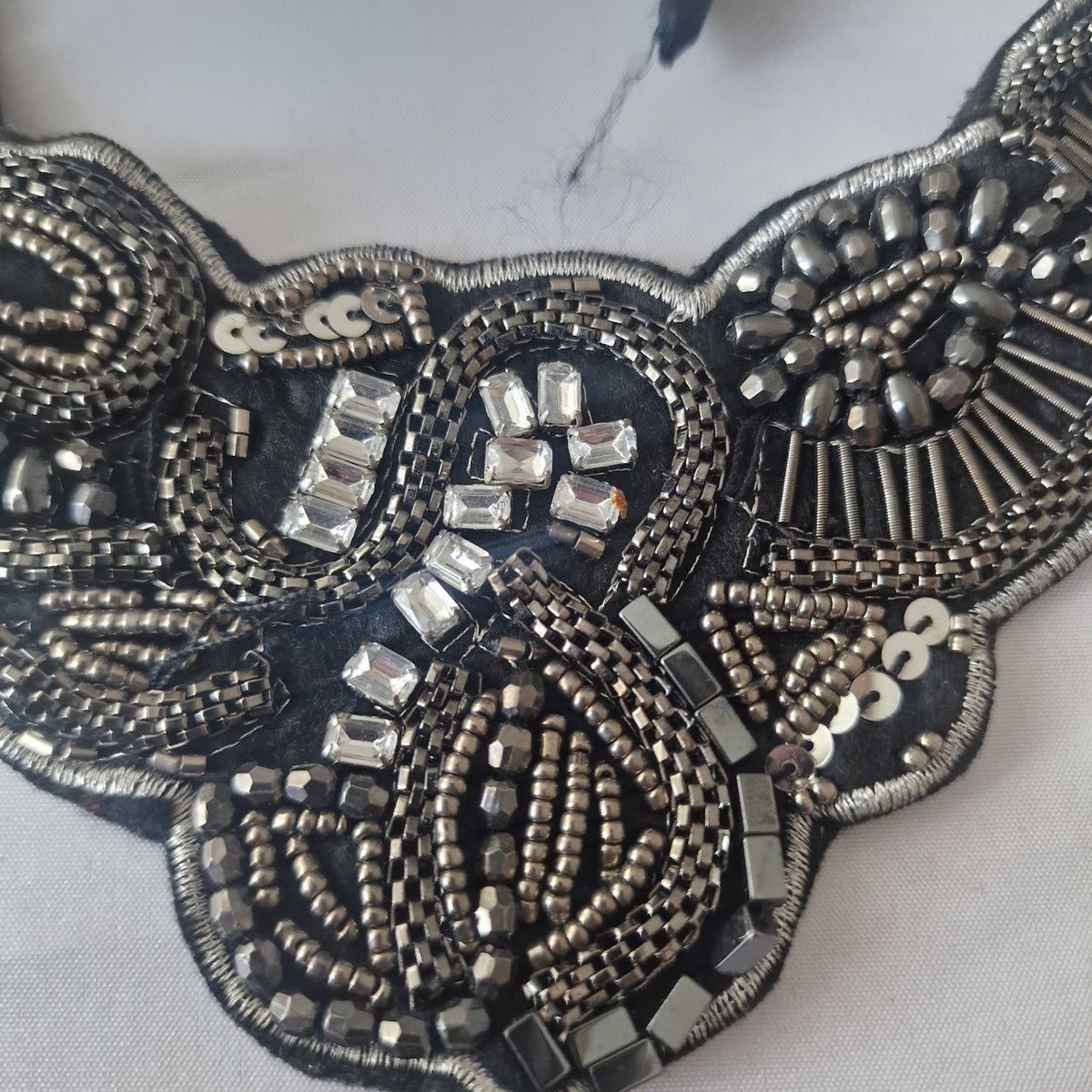 Close-up of silver-tone beads, sequins and clear rectangular accents on black bib necklace