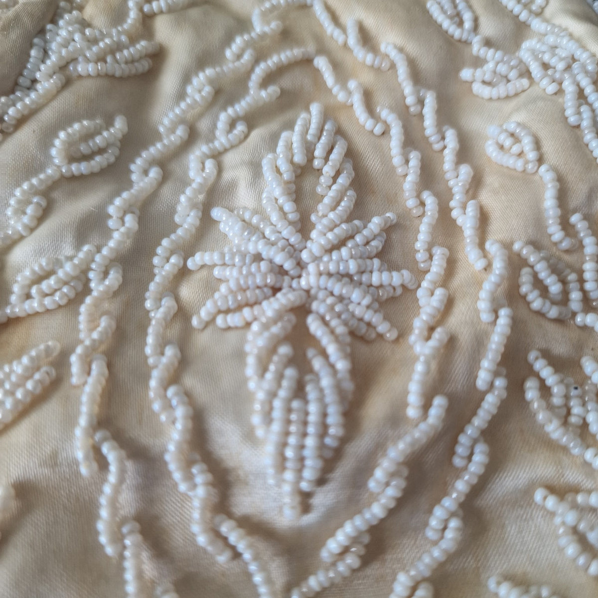 Close-up of floral seed bead embellishment on cream evening handbag